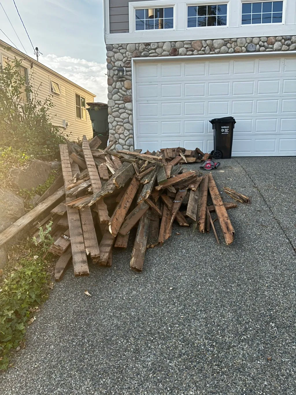 Pile of broken-down deck framing and logs stacked in a driveway