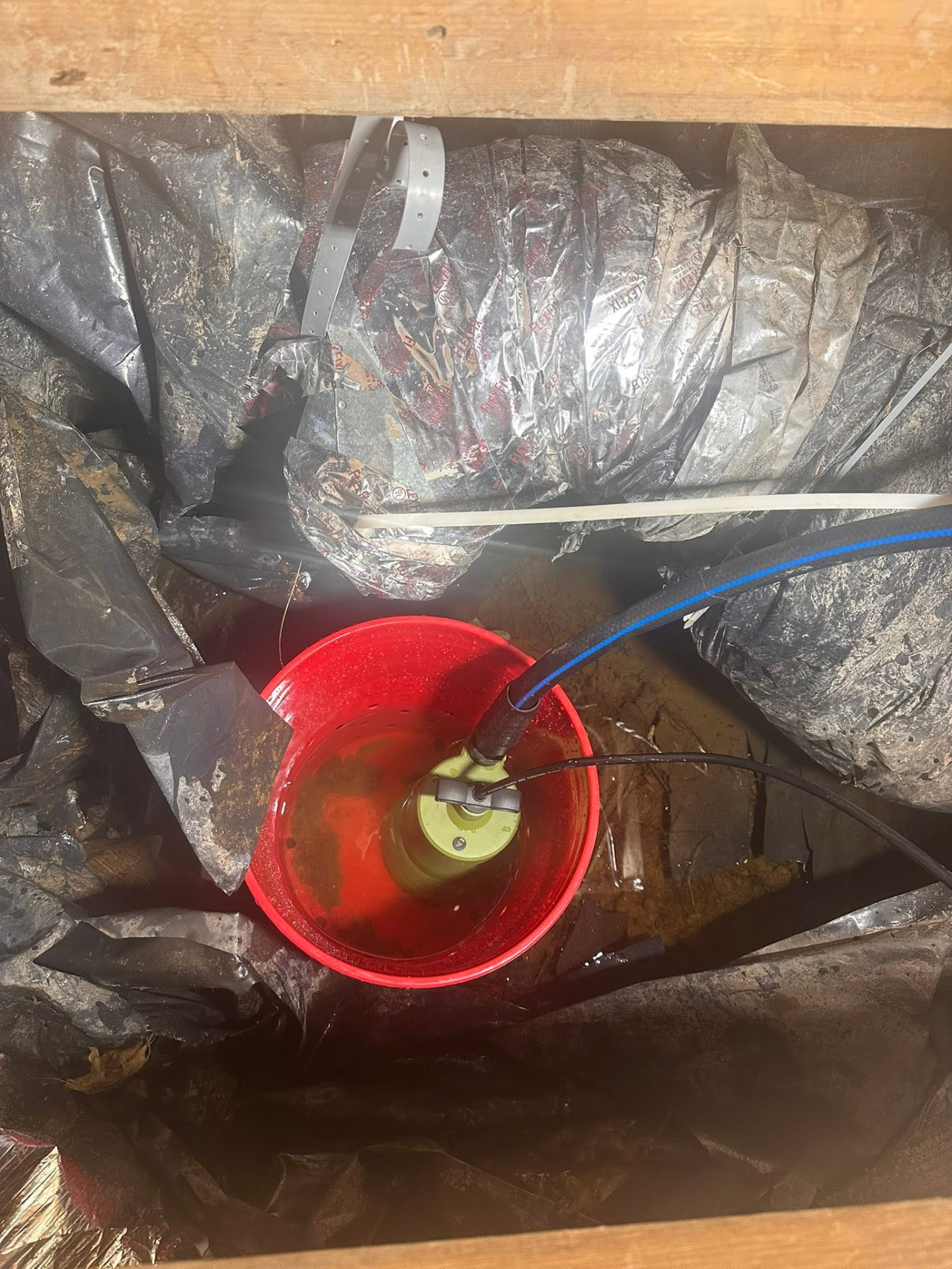 Sump pump in a red bucket removing water from a crawlspace