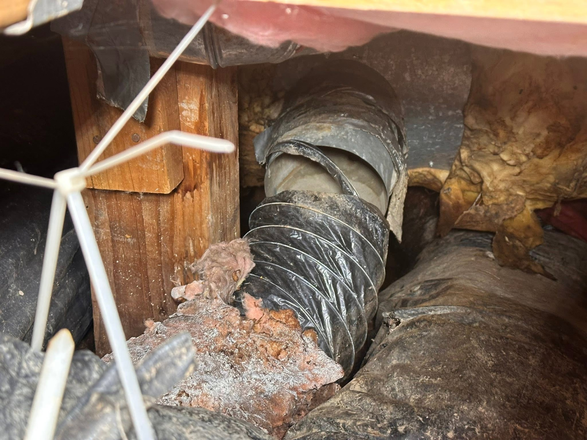 Old failing flex duct wrapped in tape inside a wet crawlspace