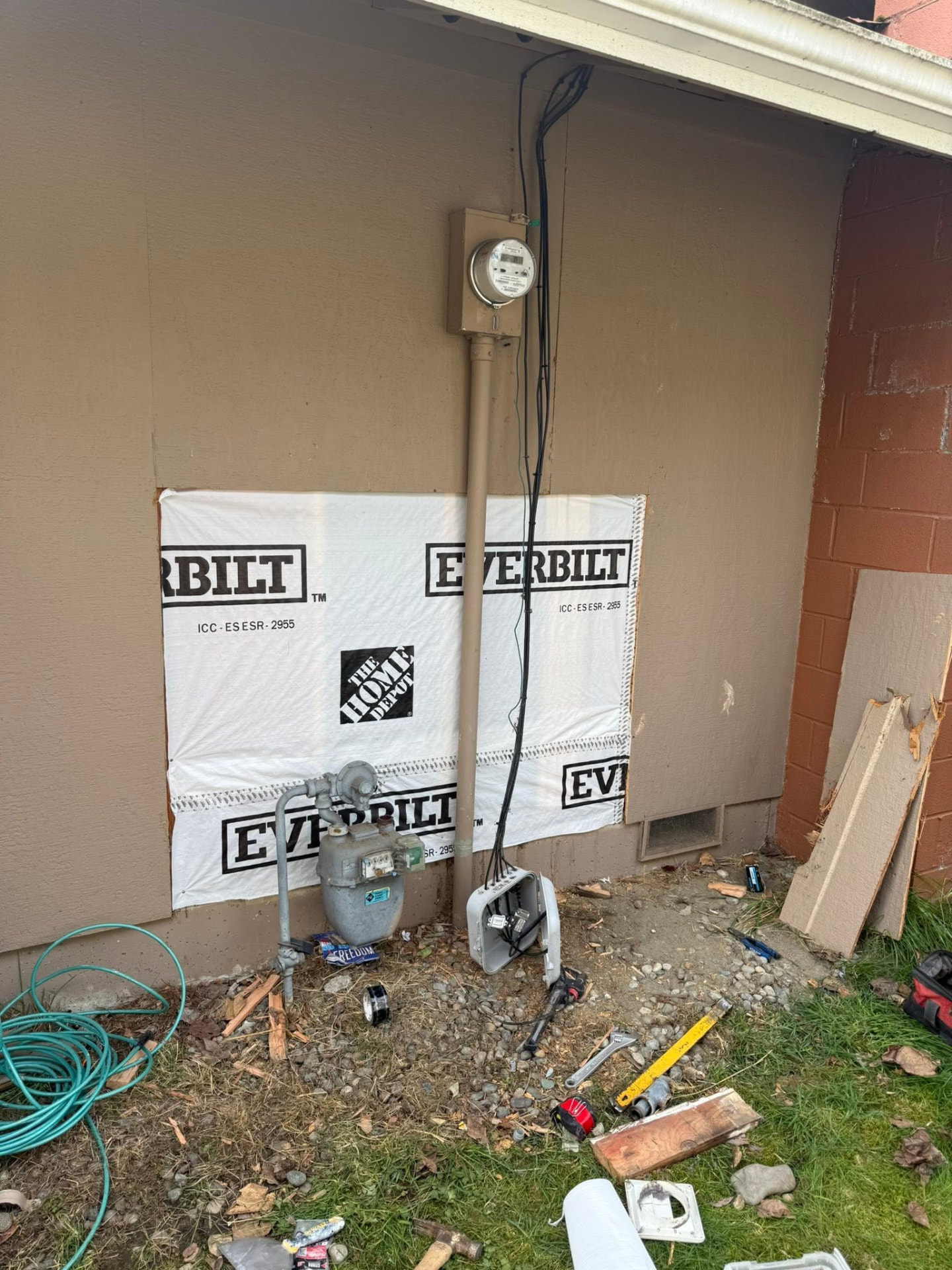 Exterior wall with new weather barrier around the gas and electric meters