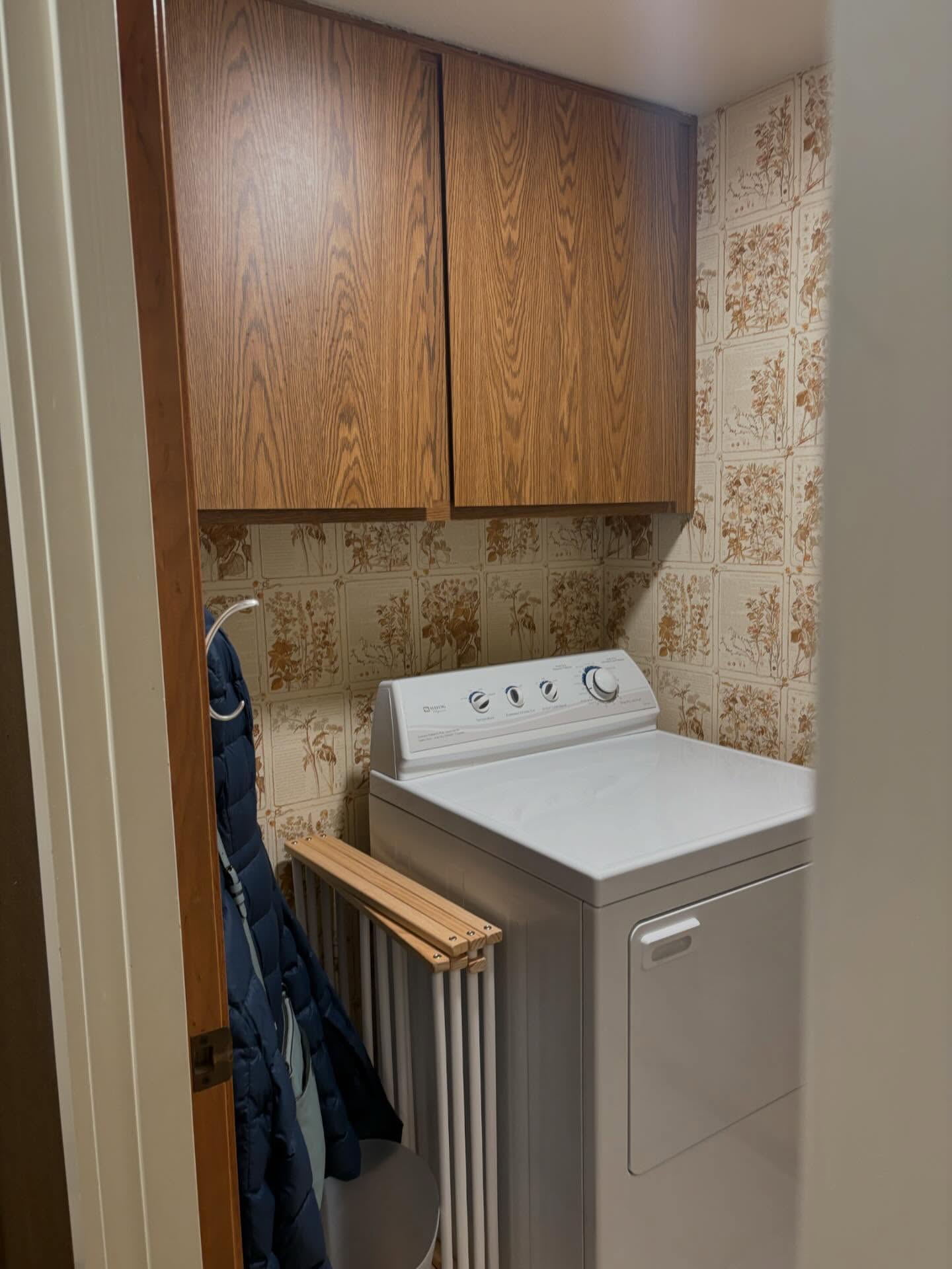 Dated laundry closet with 1970s floral wallpaper and oak cabinets