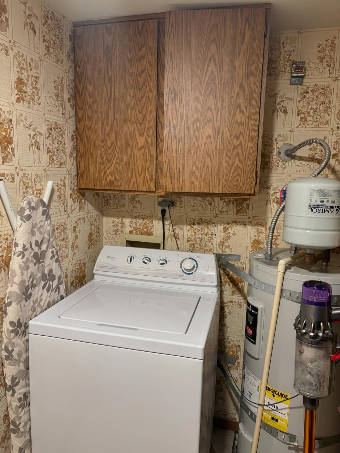 Laundry room with old water heater, ironing board and dated wallpaper